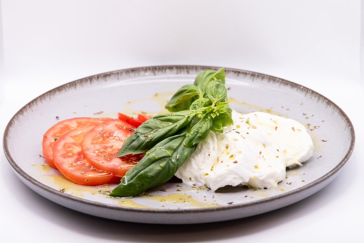 Piatto con pomodoro a fette, mozzarella fresca e foglie di basilico